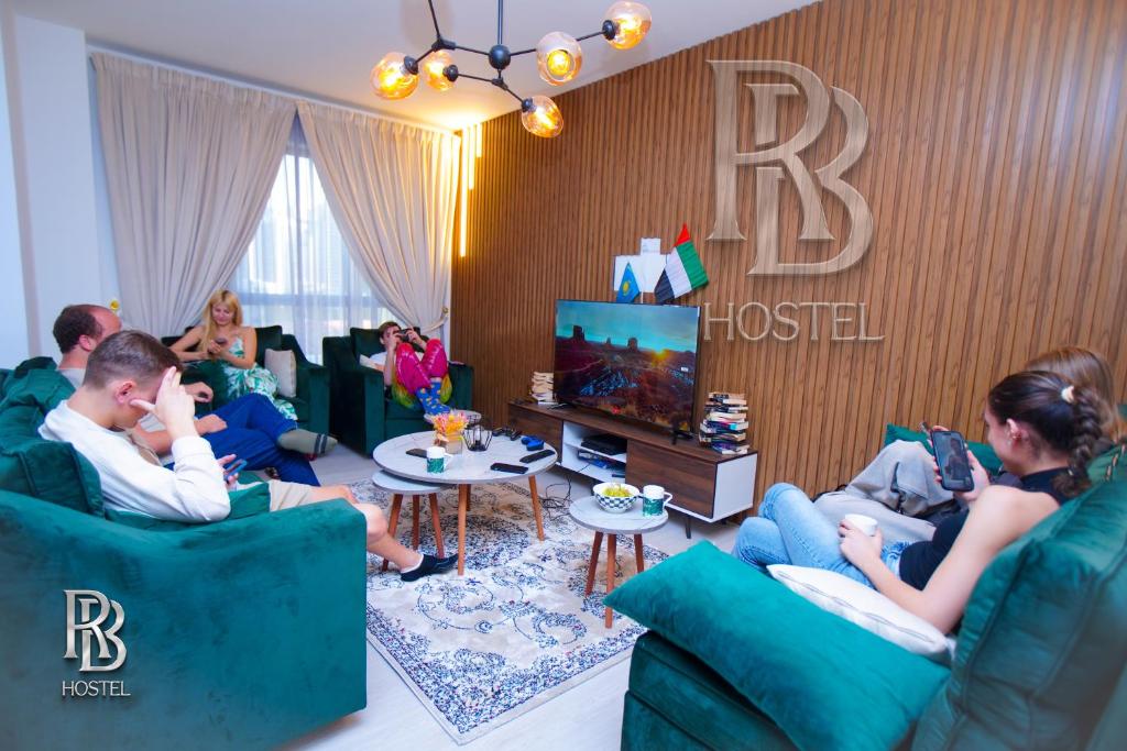 um grupo de pessoas sentadas numa sala de estar a ver televisão em Rb Hostel Jbr em Dubai