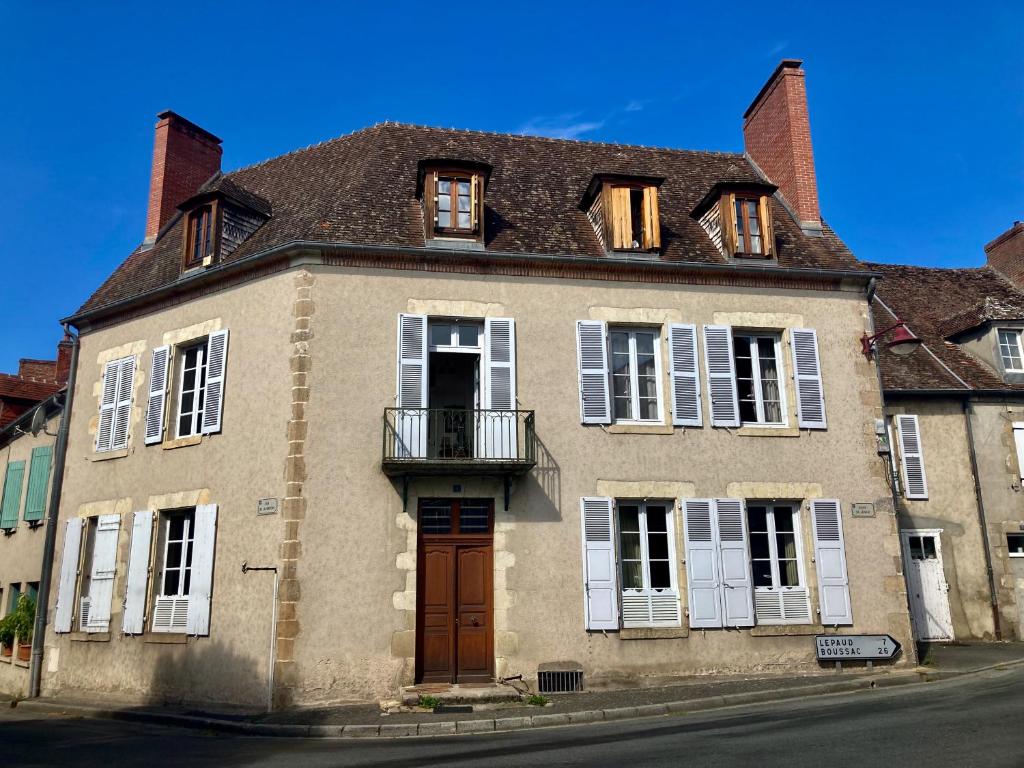 una casa antigua con ventanas blancas y una puerta marrón en La Grande maison, en Chambon-sur-Voueize