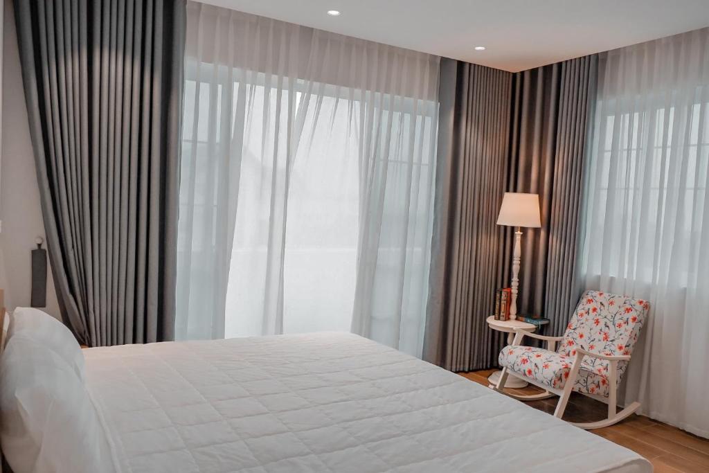 um quarto com uma cama, uma cadeira e uma janela em Lucia Villa - Melorita Hòa Lạc em Hanói