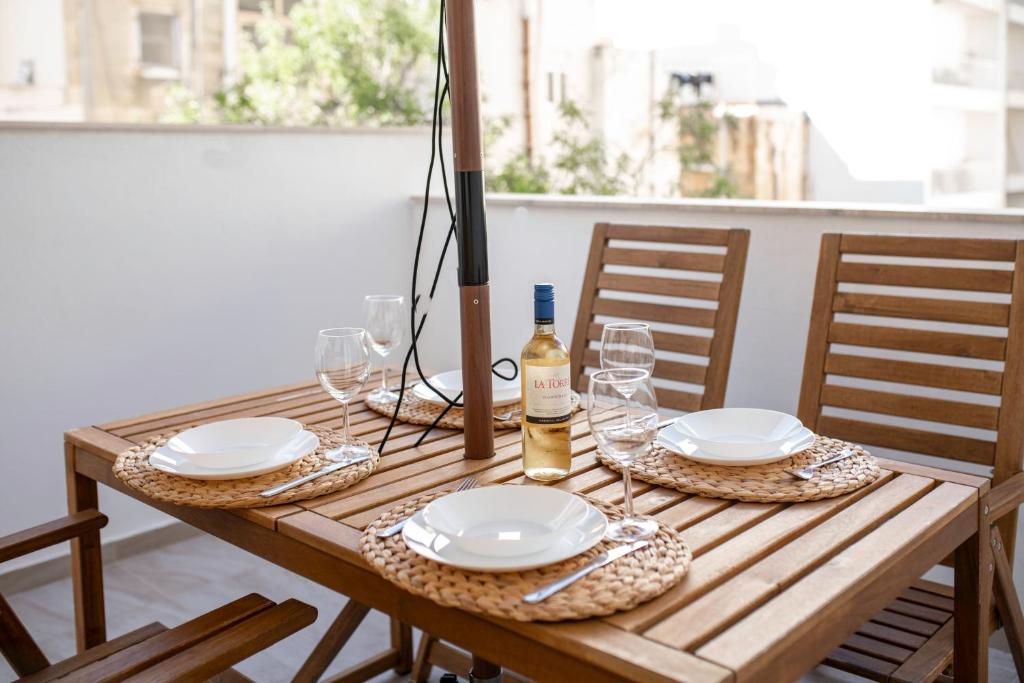 a wooden table with plates and glasses and a bottle of wine at Brand New 2 Bed 2 Bath Apartment In Sliema By The Sea in Sliema