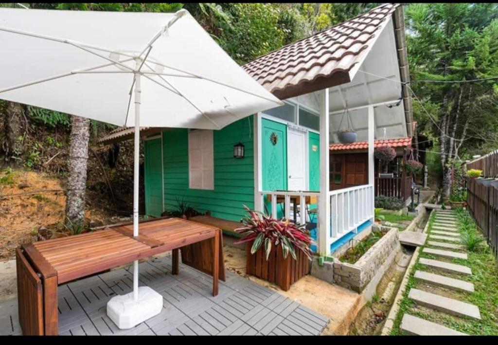 a green house with a table and an umbrella at Hillside cottage chalet studio in Tanah Rata