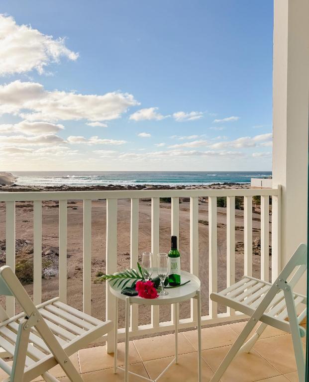 a table with a bottle of wine on a balcony with the beach at Papaya Apartments Boa Vista in Sal Rei