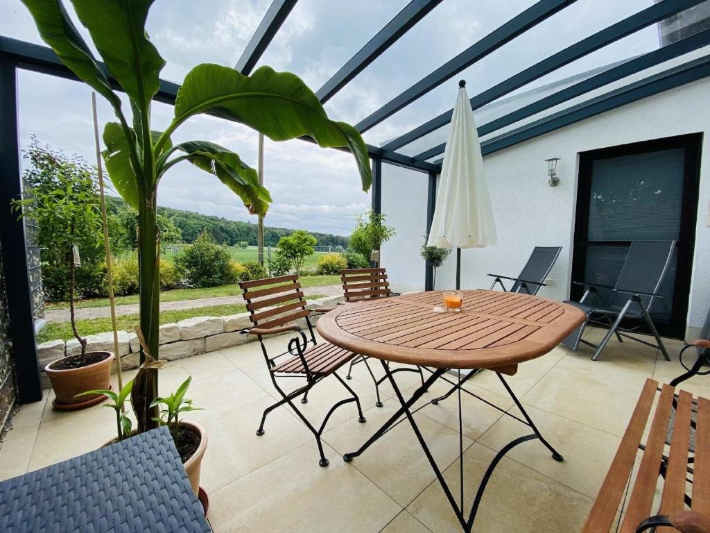 einen Wintergarten mit einem Holztisch und Stühlen auf einer Terrasse in der Unterkunft Helle Ferienwohnung in Oberfellendorf mit Terrasse, Grill und Garten in Oberfellendorf