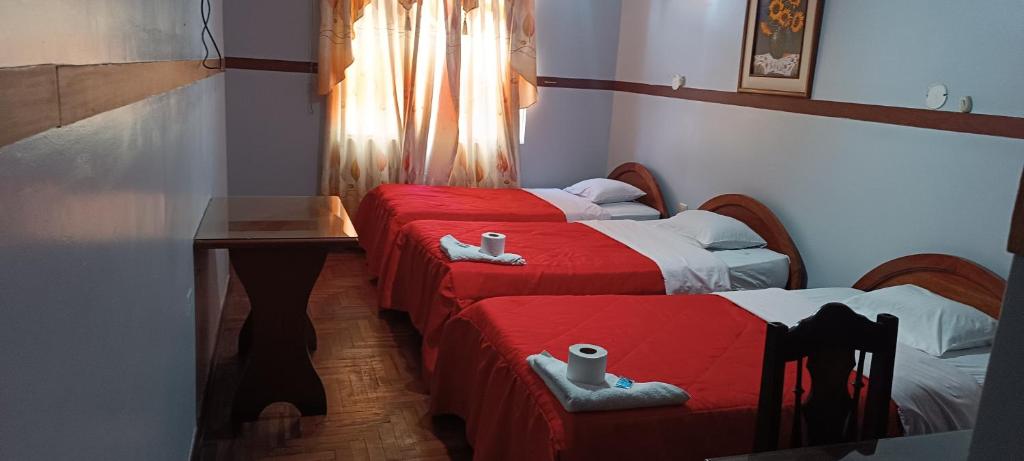a room with two beds with red sheets and a table at HOTEL LAS GARDENIAS in Trujillo