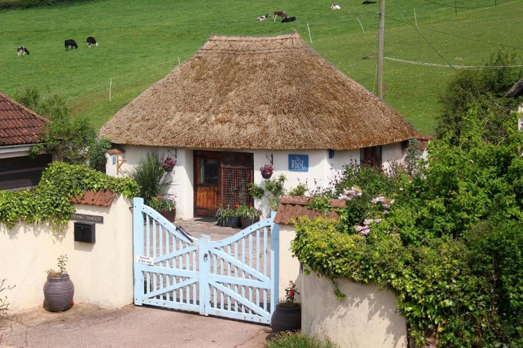 Cette petite maison dispose d'un toit de chaume et d'un portail blanc. dans l'établissement Ferienhaus für 2 Personen ca 50 qm in Stokeinteignhead, England Südküste von England, à Stokeinteignhead