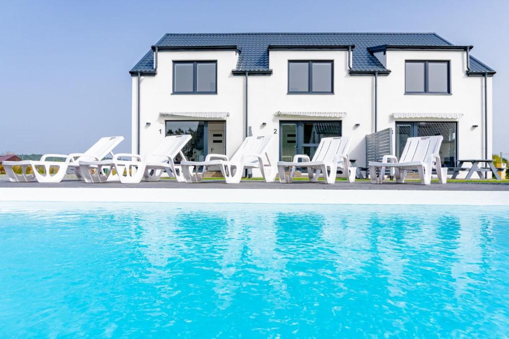 una casa con sillas blancas y piscina en Cichy Domek Apartamenty - Podgrzewany Basen en Karwia