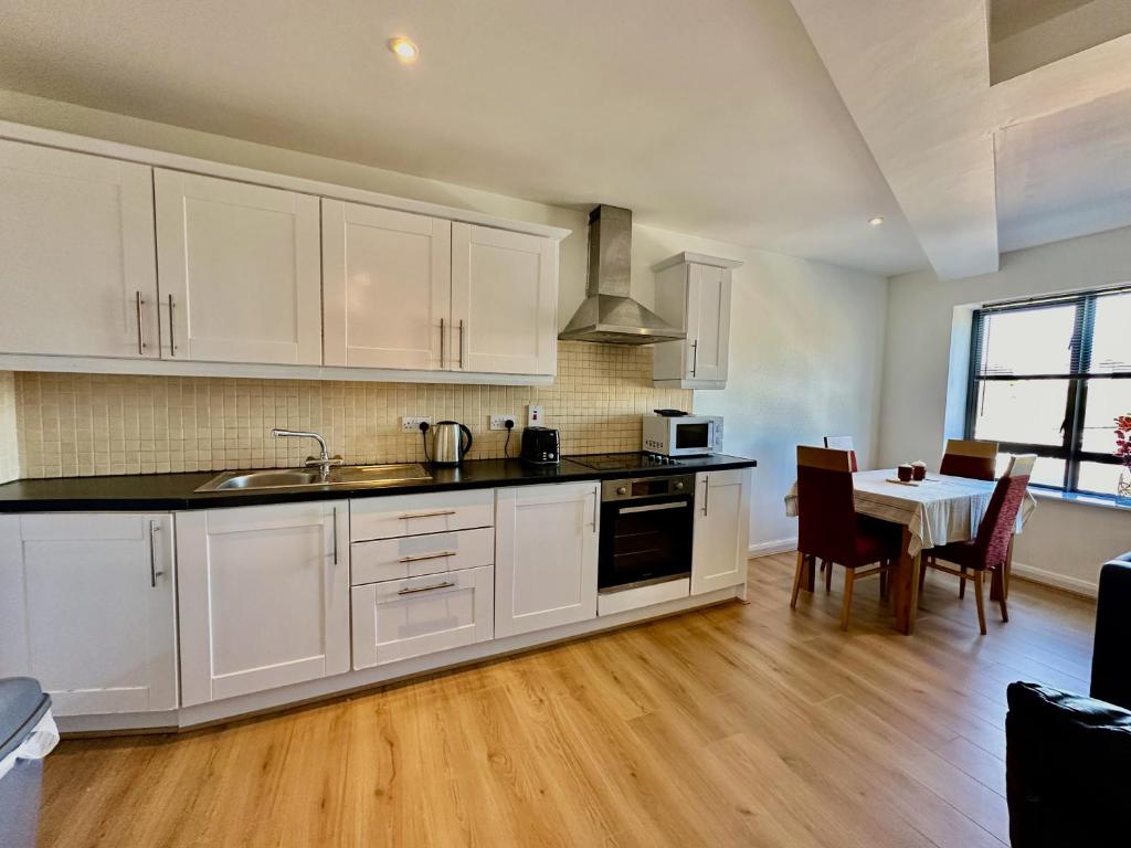 una cocina con armarios blancos y una mesa con sillas. en Wellington Central Apartment en Waterford