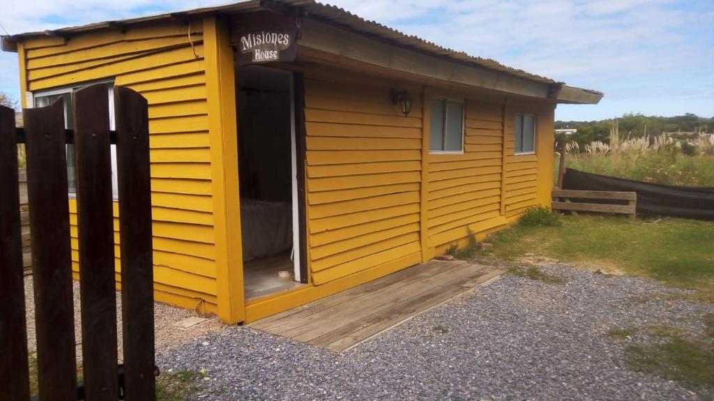 uma pequena casa amarela com um deque de madeira em Cabaña de playa em Balneario Buenos Aires