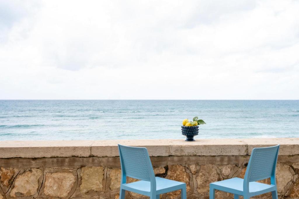 two blue chairs sitting on a wall near the ocean at Le Mura - Melilli in Trapani