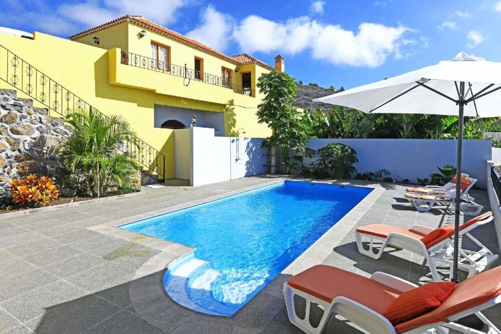 a swimming pool with chairs and an umbrella and a house at Ferienhaus für 6 Personen ca 105 qm in La Punta, La Palma Westküste von La Palma in Tijarafe