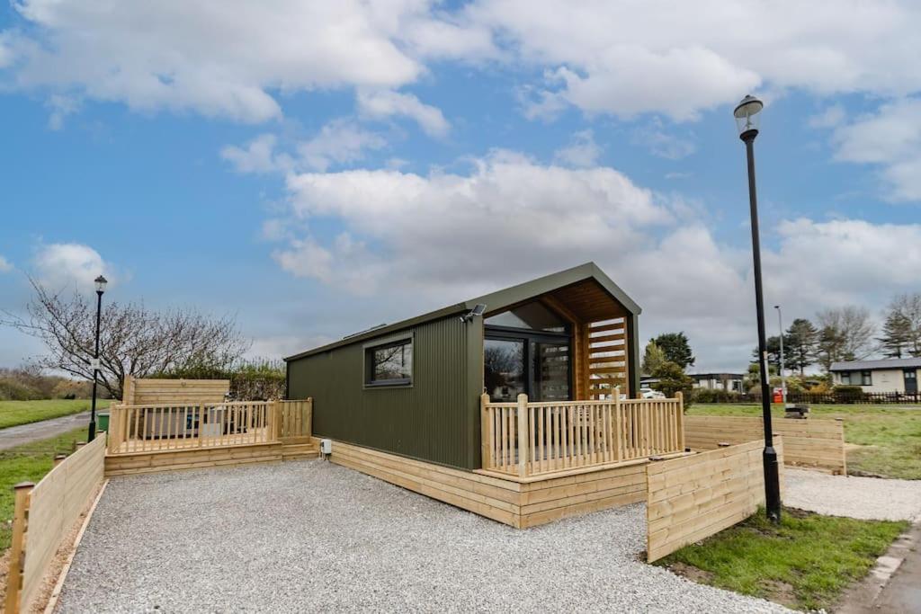 a small green cabin with a wooden deck at Lowfield Lodge & Hot Tub - Humberston Fitties Beach in Cleethorpes