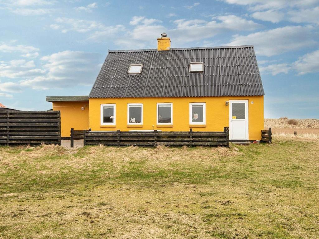 una casa amarilla con techo negro en un campo en 6 person holiday home in Harbo re en Harboør