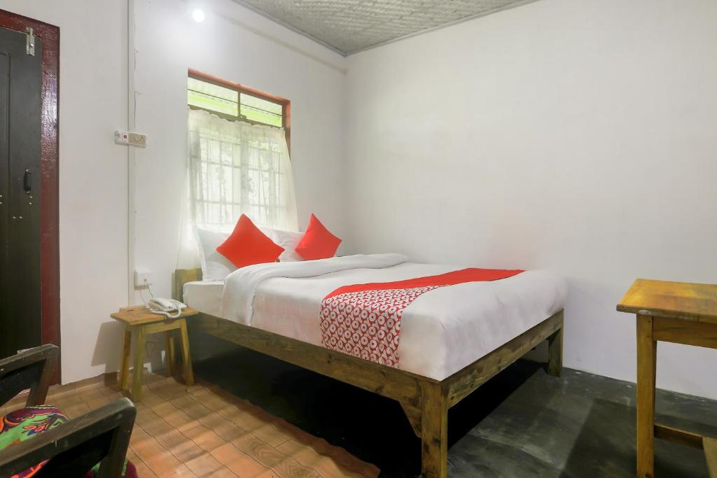 a bedroom with a bed with red pillows and a window at OYO Bell's Bigxa Homestay in Cherrapunji
