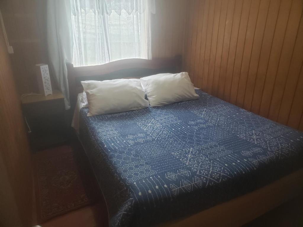 1 cama con 2 almohadas y manta azul en Cabaña Alejandra, en Puerto Puyuhuapi