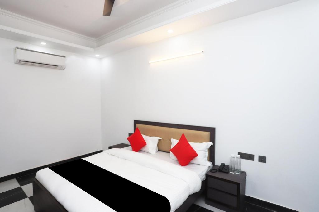 a white bedroom with a bed with red pillows at Capital O Peaceful Stays Near ISKCON Temple Noida in Noida