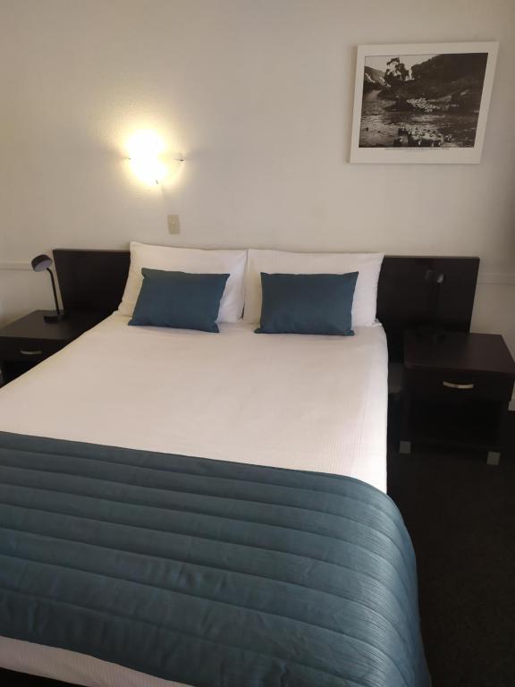 a bedroom with a large bed with blue pillows at Alexander Motel in Taumarunui