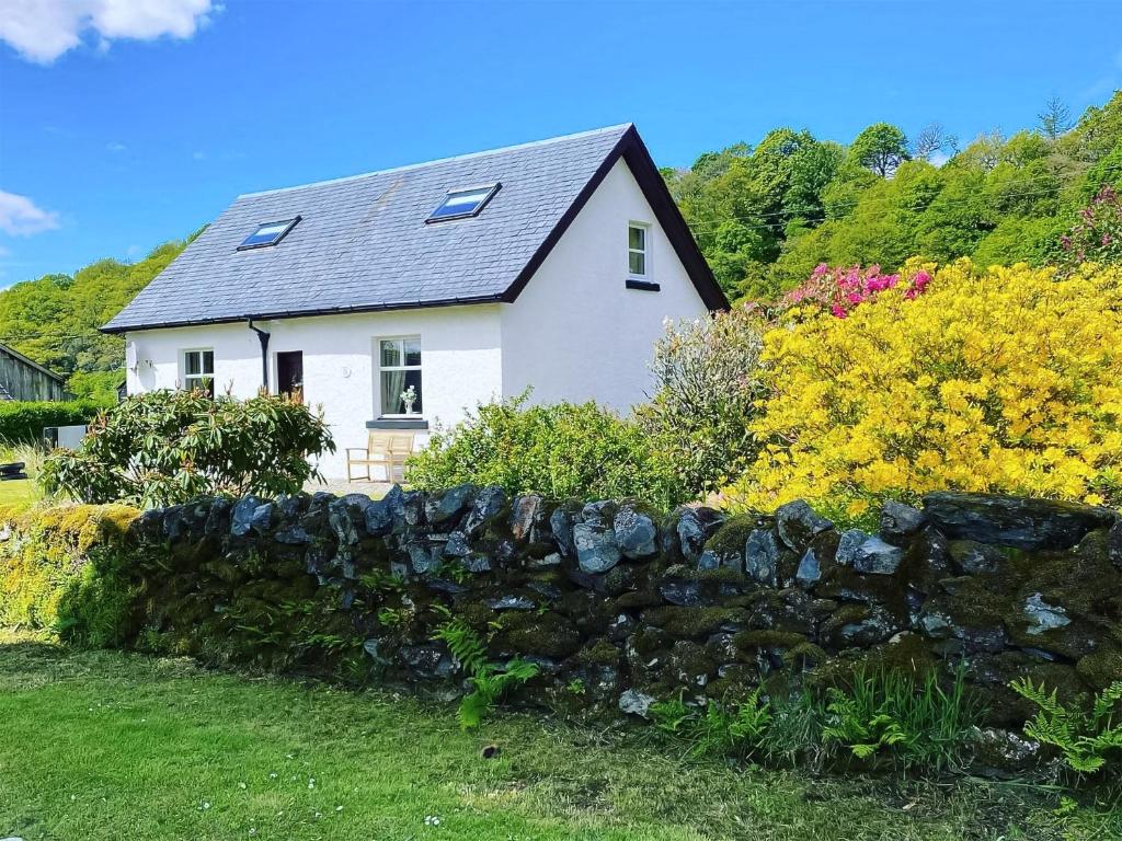 a white house behind a stone wall at Kirnan Cottage in Kilmichael Glassary