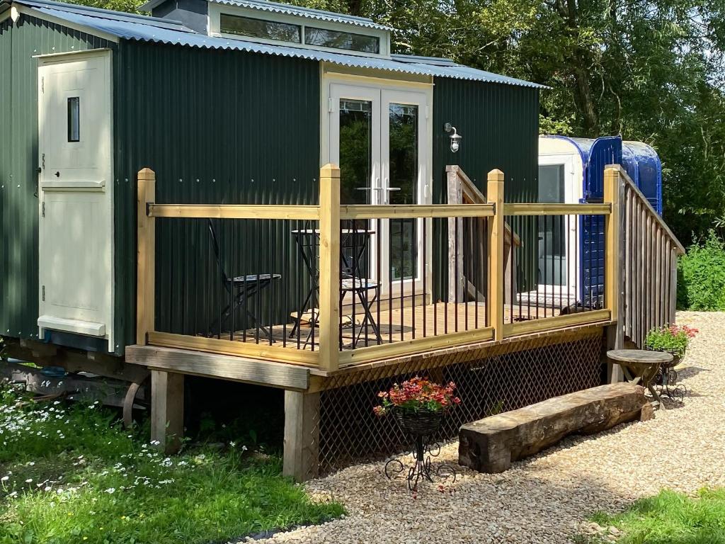 una casa verde con terraza con mesa en Ivy Shepherds Hut - Uk45590 en Seend