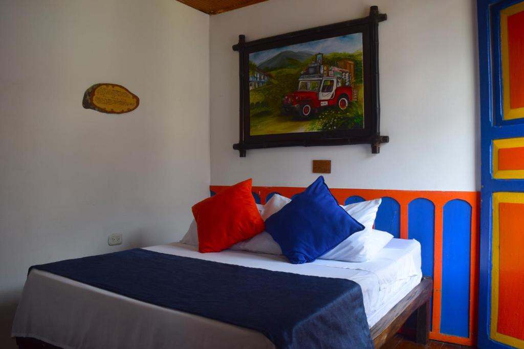 ein Bett mit bunten Kissen und ein Gemälde an der Wand in der Unterkunft FILANDIA HOTEL in Filandia