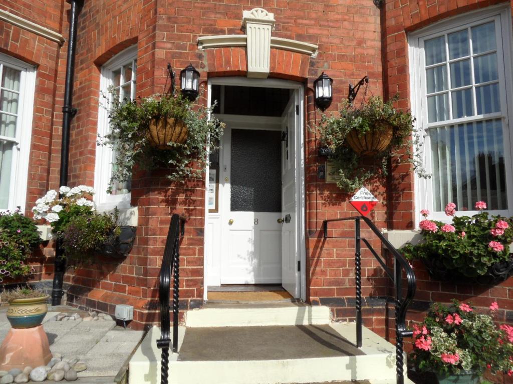 a brick house with a white door and flowers at Glenora Guest House in Whitby