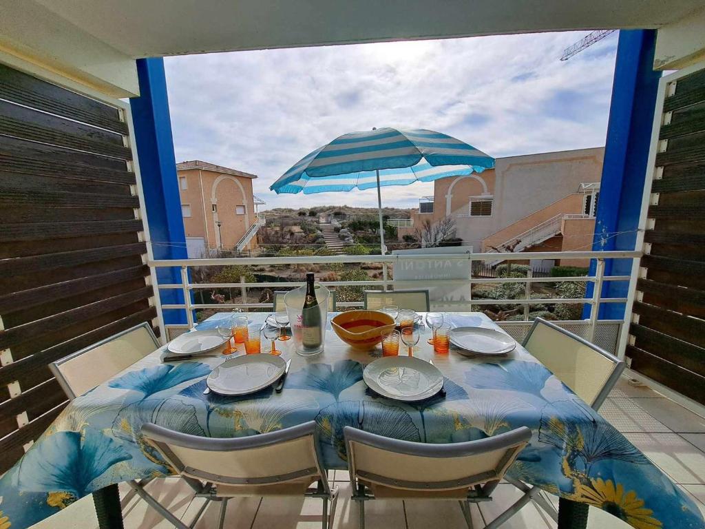 una mesa con sillas y una sombrilla en el balcón en Appartement Marseillan-Plage, 2 pièces, 6 personnes - FR-1-326-816, en Marseillan