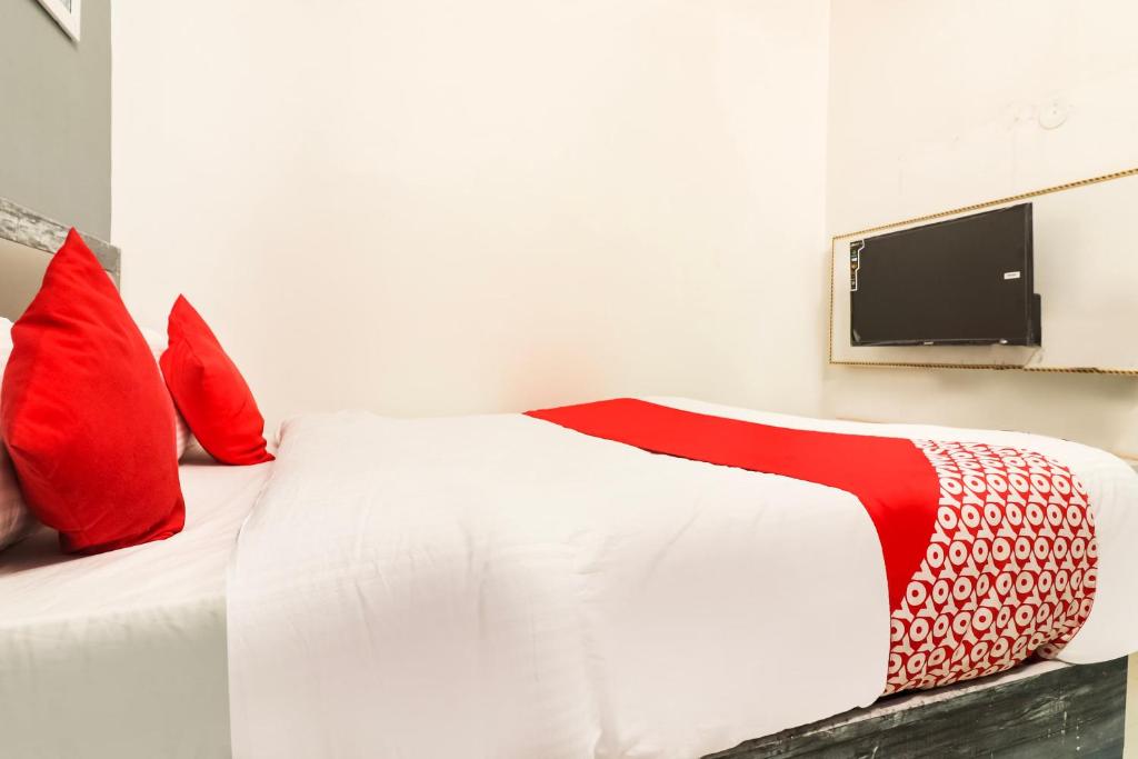 Elle comprend un lit blanc avec des oreillers rouges et une télévision murale. dans l'établissement Hotel Sheela, à Rohtak