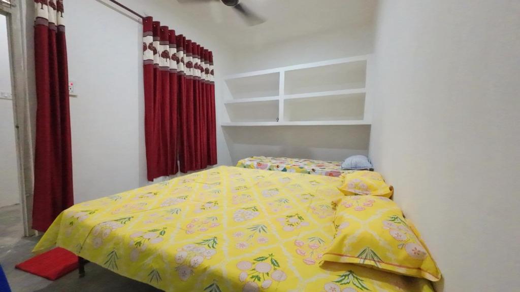 1 dormitorio con cama amarilla y cortinas rojas en Maharishi Valmiki Homestay, en Ayodhya