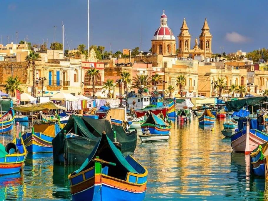 eine Gruppe von Booten, die in einem Hafen mit Gebäuden angedockt sind in der Unterkunft Bluemoon Apartment in Marsaxlokk