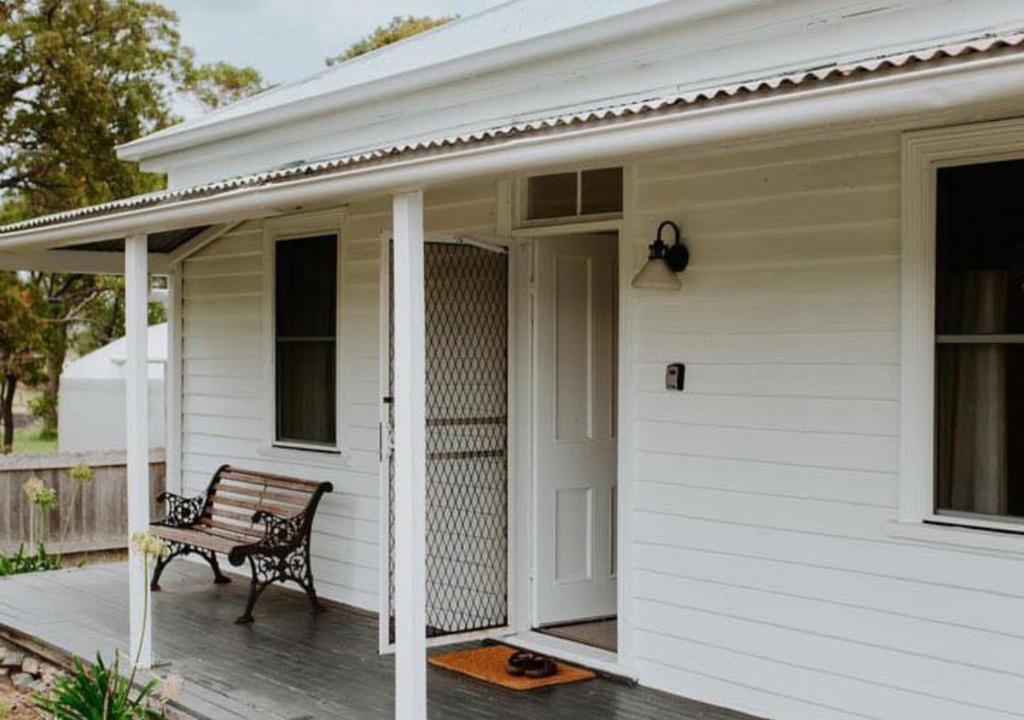 eine Bank auf der Veranda eines weißen Hauses in der Unterkunft Falmouth Cottage - Dog Friendly Beachside Getaway 2,5 Acres in Falmouth