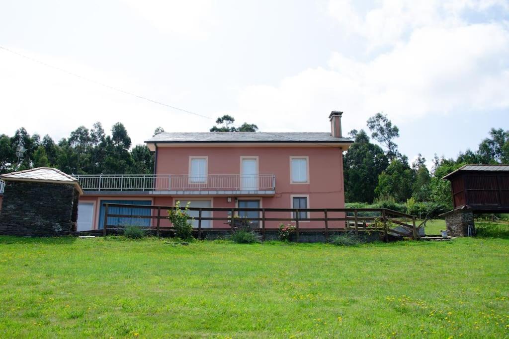 una casa rosa con un campo verde delante de ella en Villa Montedonigo, en Loiba