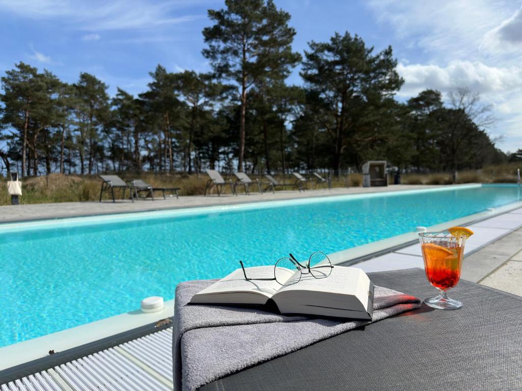 a book and glasses on a table next to a swimming pool at Inselloft Rügen - Meerblick, Pool & eigener Strandzugang in Binz