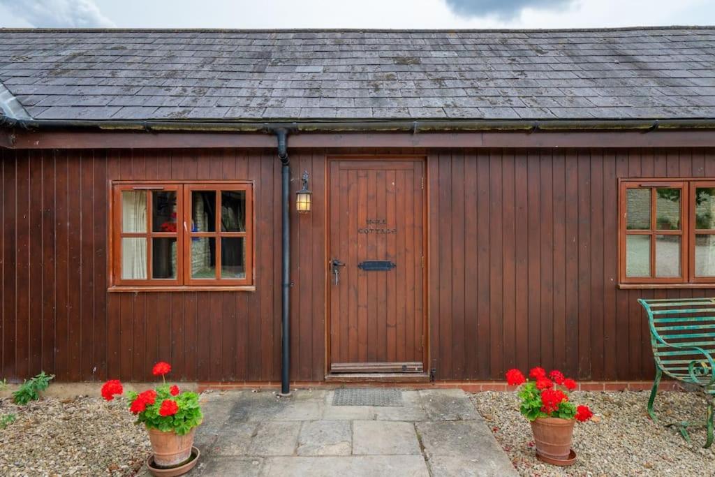 a wooden shed with a wooden door and flowers at Well Cottage - Compact & Cosy! in Buckinghamshire