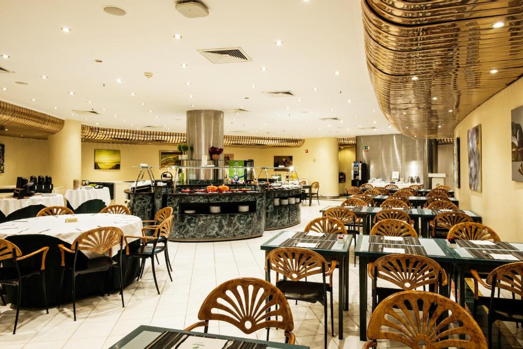 A bright dining room is arranged around a central buffet island with many small tables.