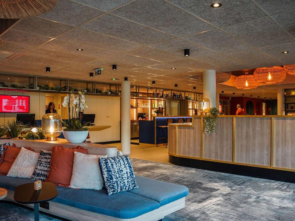 - un hall avec un canapé bleu et un bar dans l'établissement ibis Bayeux Port En Bessin, à Port-en-Bessin-Huppain