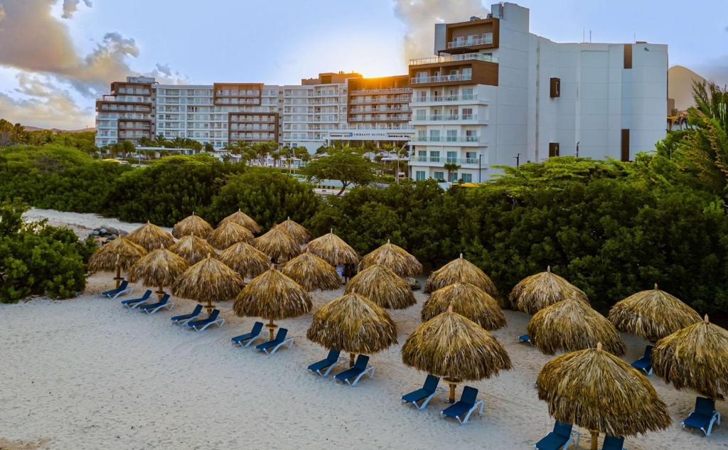 eine Gruppe Strohschirme und -stühle am Strand in der Unterkunft Embassy Suites By Hilton Aruba Resort in Palm-Eagle Beach