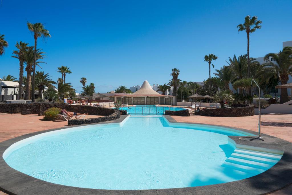 a large swimming pool in a resort with palm trees at Lanzahost Casa Sunny Seafront in Costa Teguise