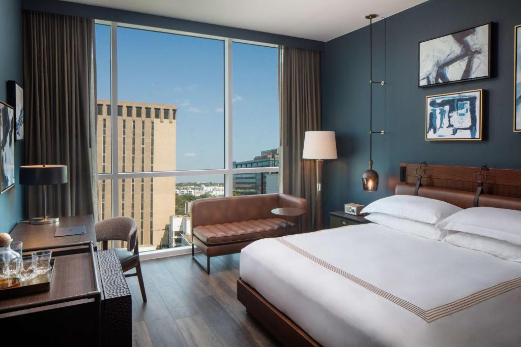 サンアントニオにあるThompson San Antonio - Riverwalk, by Hyattのベッドと大きな窓が備わるホテルルームです。
