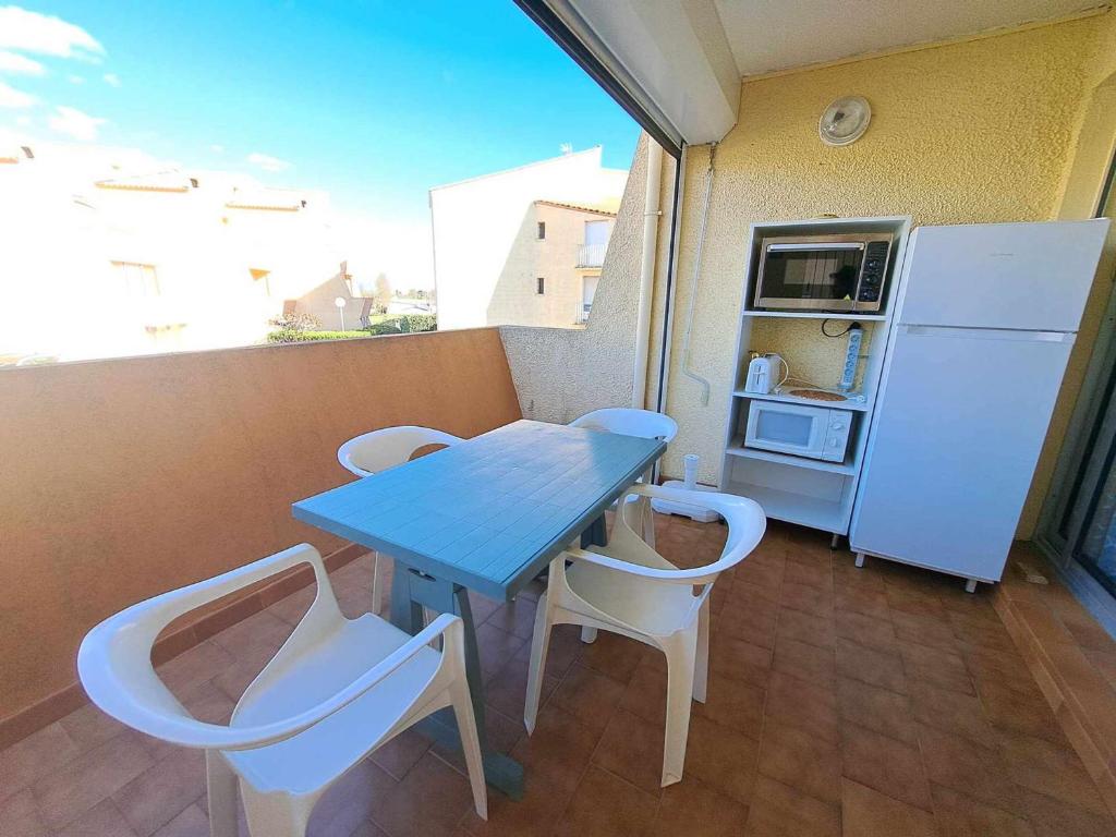 d'un balcon avec une table et des chaises bleues et un réfrigérateur. dans l'établissement Studio cosy 4 pers avec terrasse, parking sécurisé, proche commerces à Marseillan - FR-1-326-591, à Marseillan