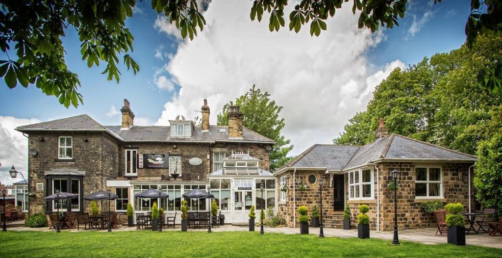 an exterior view of a large stone house with umbrellas at Dimple Well Lodge Hotel in Wakefield