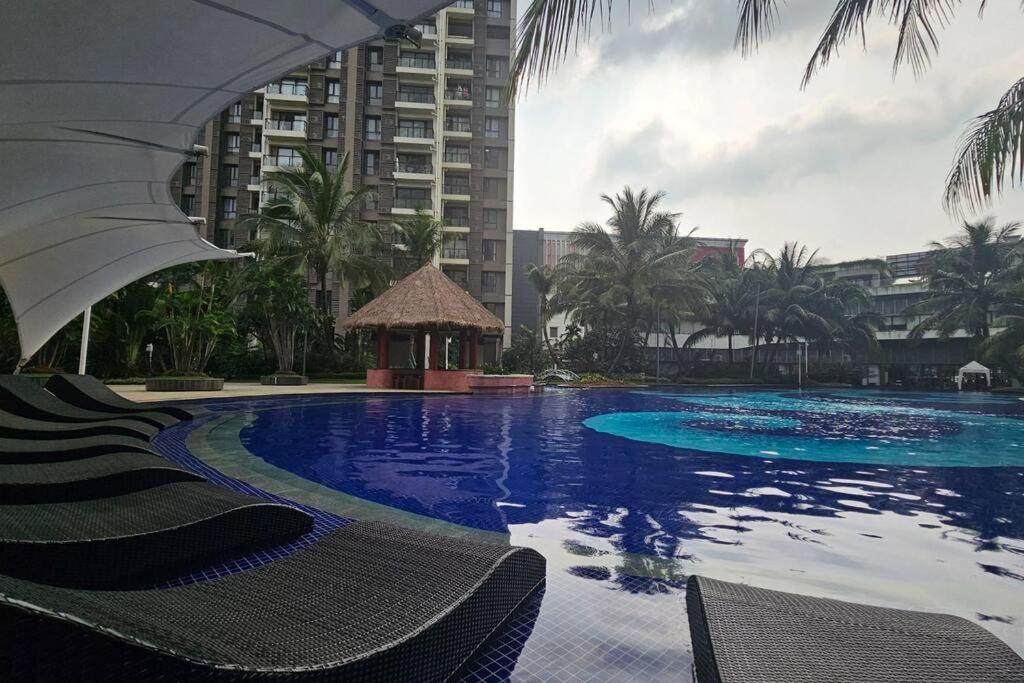 a large swimming pool with chairs and an umbrella at Sky House BSD Apartemen T.Duxton in Tjilandak