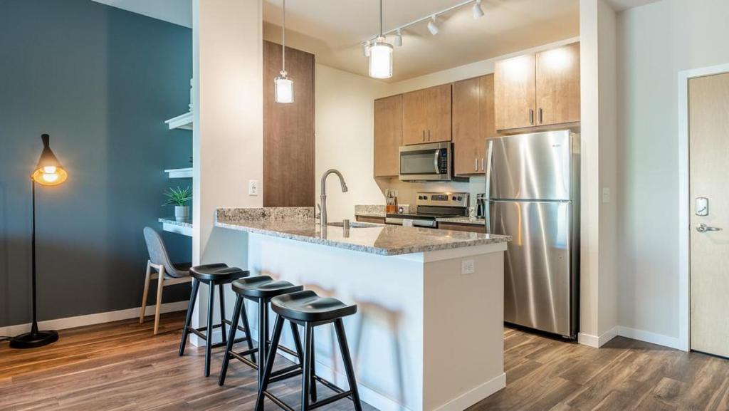 a kitchen with a counter with stools and a refrigerator at Landing at Three Rivers - 1 Bedroom in Central Fort Wayne in Fort Wayne