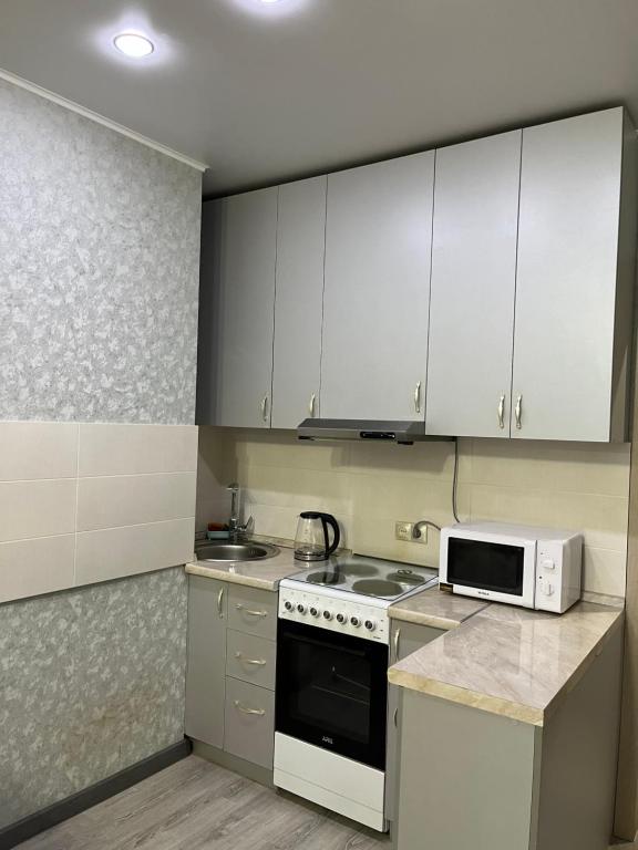 uma cozinha com armários brancos, um fogão e um micro-ondas em 2 комнатная за Хан шатыром левый берег em Taldykolʼ