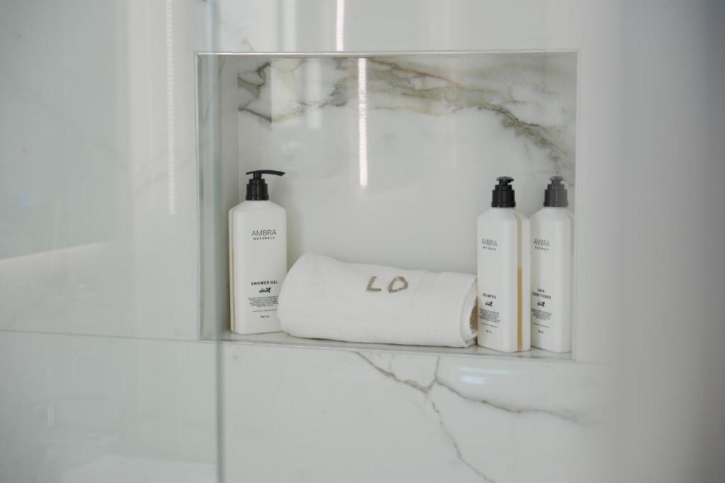 a shelf with four bottles of soap and towels at Loutsiana Deluxe Apts in Ayia Napa
