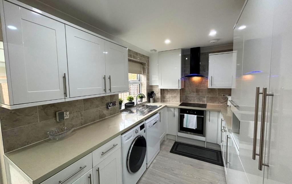 a white kitchen with white cabinets and a dishwasher at Addlestone Stylish Spacious Three Bedroom House in Addlestone