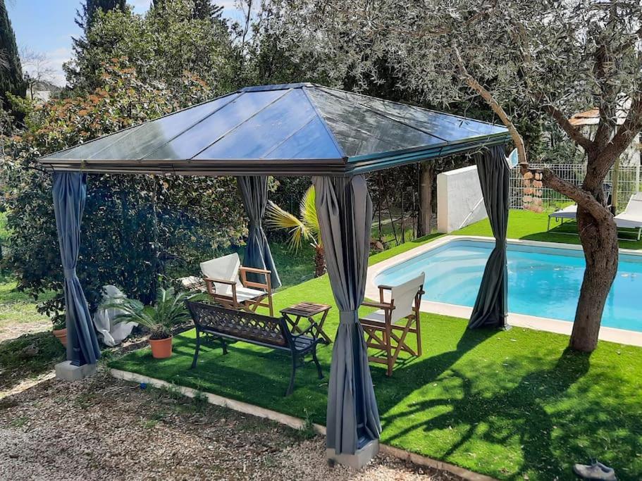 een prieel met stoelen en een tafel naast een zwembad bij Villa climatisée piscine in Montpellier