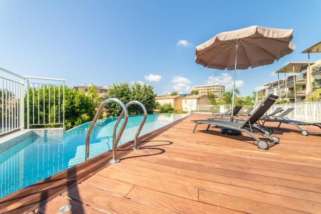 a swimming pool with an umbrella and a chair and a desk at Séquoia furnished apartment in Antibes