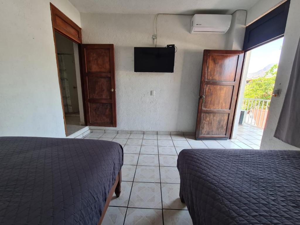 a bedroom with two beds and a tv and a door at Hotel del Callejón in Zihuatanejo