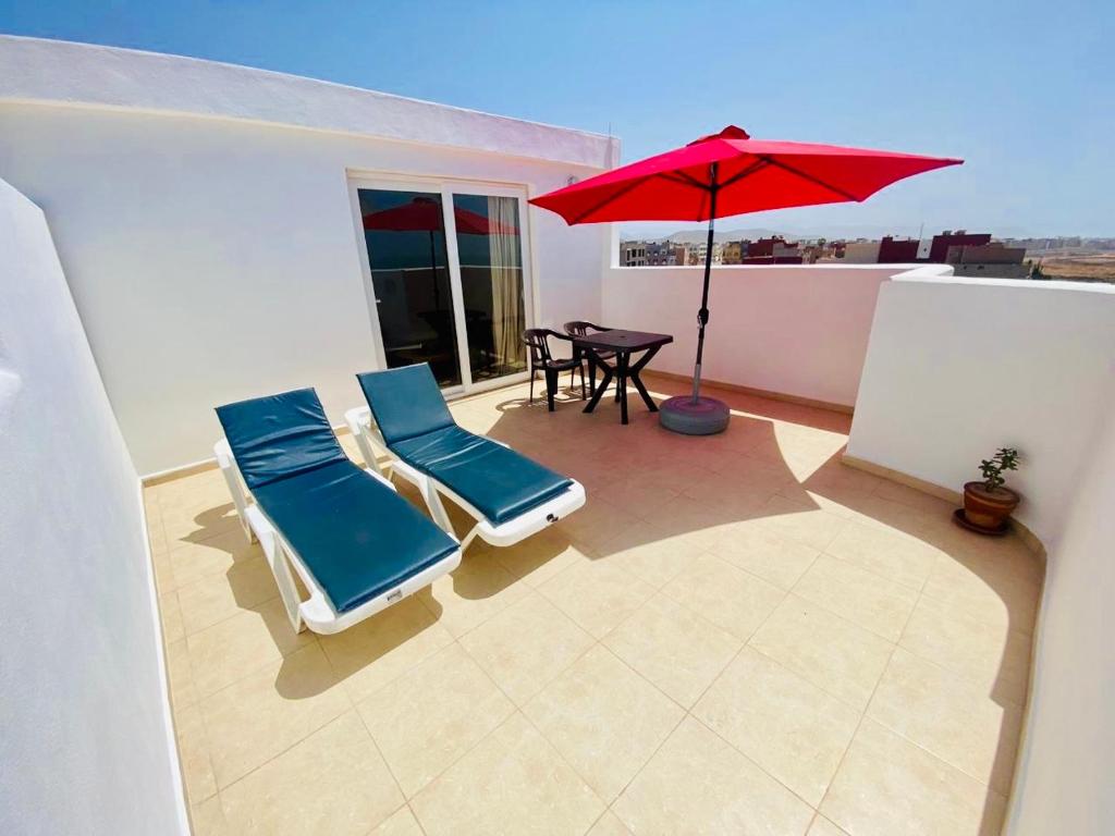 a patio with two chairs and a red umbrella at Amazigh Home in Mirleft