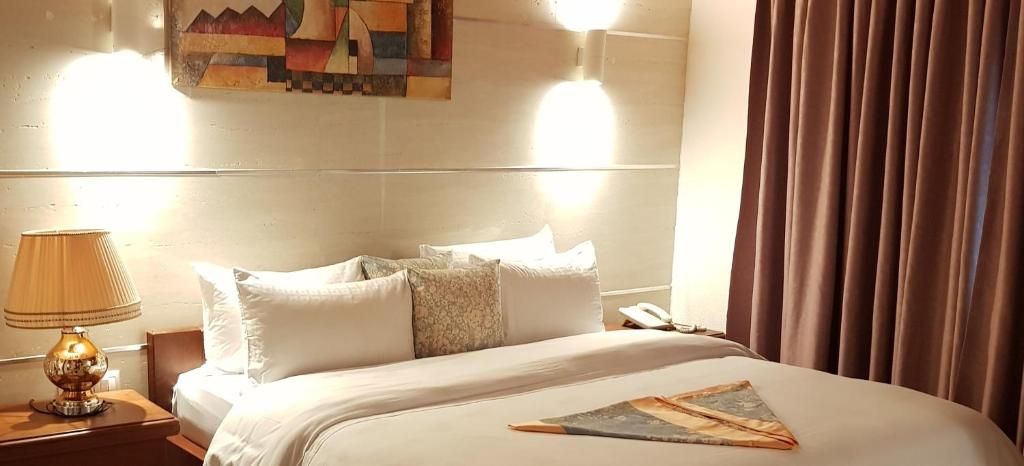 1 dormitorio con 1 cama grande con sábanas y almohadas blancas en ADAMAOUA GRAND HOTEL AKWA, en Douala