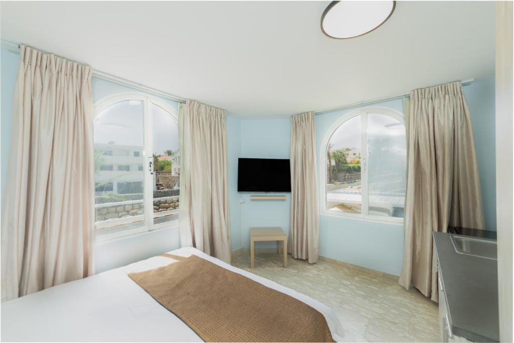 a bedroom with a bed and a tv and two windows at Villa Li Eilat in Eilat
